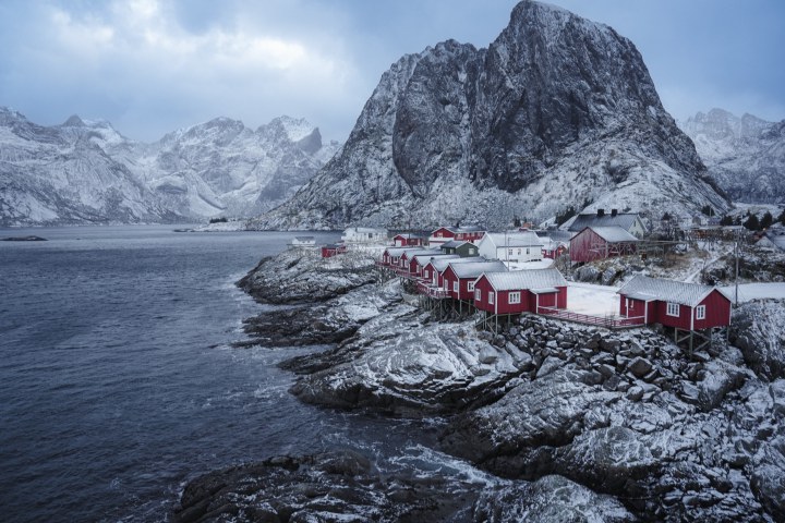 Red cabins along a rocky coast beneath snow-covered mountains