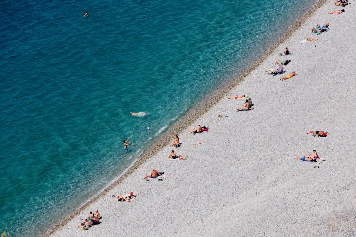 Beachgoers along a pale shoreline beside clear turquoise water